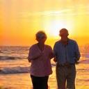 Pareja de adultos mayores sonriendo y disfrutando de un atardecer en la playa, simbolizando una jubilación plena